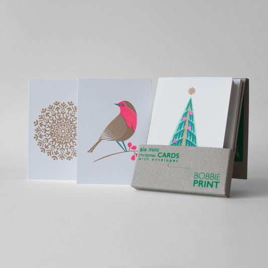 A set of six festive mini Christmas cards with envelopes, displayed in an open box that is screen printed and made from 100% recycled cardstock.
