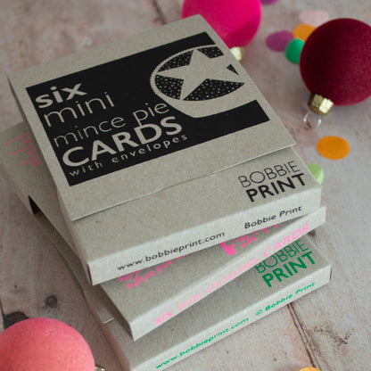 Stack of boxed Christmas cards sets by Bobbie Print on a wooden surface with colorful polka dot decorations.